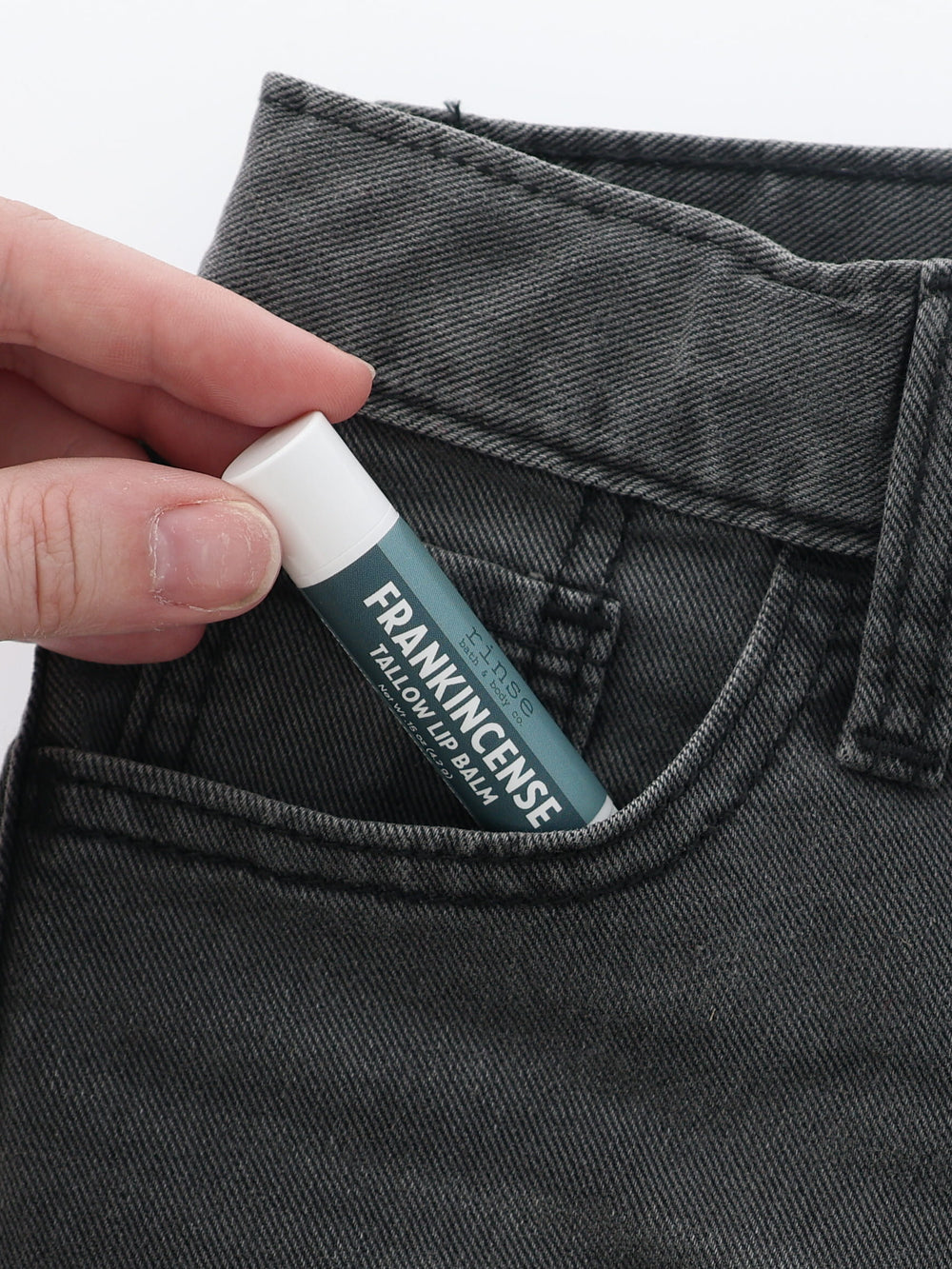 Frankincense Tallow Lip Balm half-tucked into the front pocket of charcoal jeans, held between two fingers