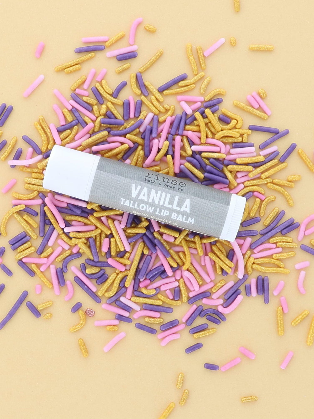 Vanilla Tallow Lip Balm tube with grey label lying on pink, purple and gold sprinkles on a butter-yellow backdrop