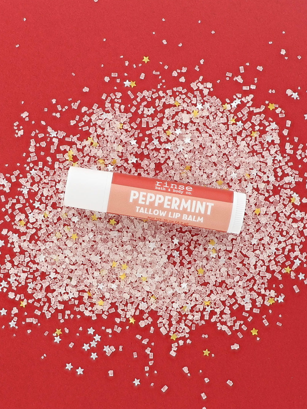 Peppermint Tallow Lip Balm tube with coral-red label lying on pink-white crystals and tiny gold and silver stars on red