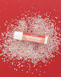 Peppermint Tallow Lip Balm tube with coral-red label lying on pink-white crystals and tiny gold and silver stars on red