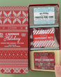 Open Handmade Holiday box on green holding Frosted Pine Cone, Peppermint Patti, and Spiced Cranberry — Fair Isle lid beside three festive bars