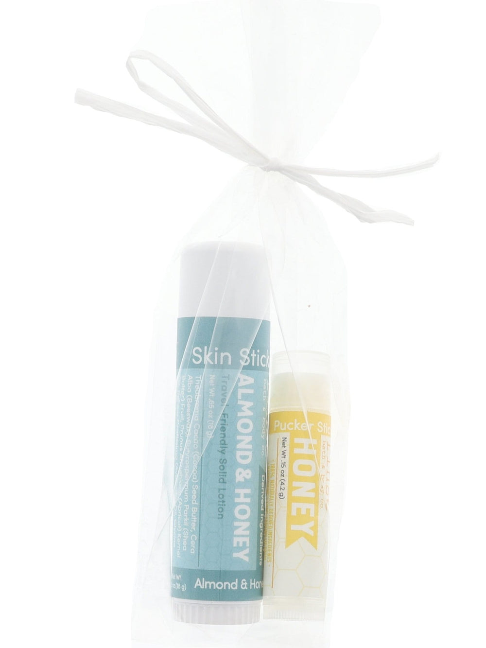 Almond & Honey Skin Stick and Honey Pucker Stick tucked in a sheer white mesh bag — gift-ready duo on bright white