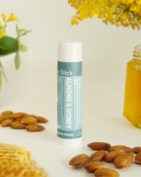 Almond & Honey solid lotion stick standing beside whole almonds and honeycomb — warm almond and honey in a twist-up bar of concentrated moisture. Rinse Bath & Body Co.
