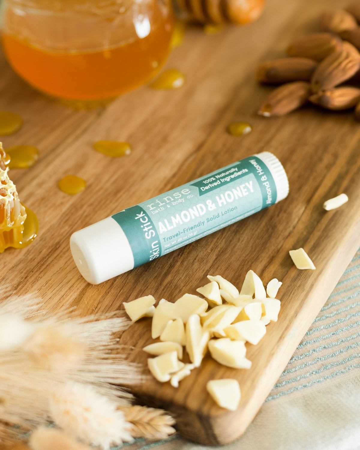 Almond & Honey Skin Stick solid lotion beside honey jar, almonds, and honeycomb on wood