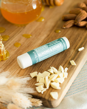 Almond & Honey Skin Stick solid lotion beside honey jar, almonds, and honeycomb on wood