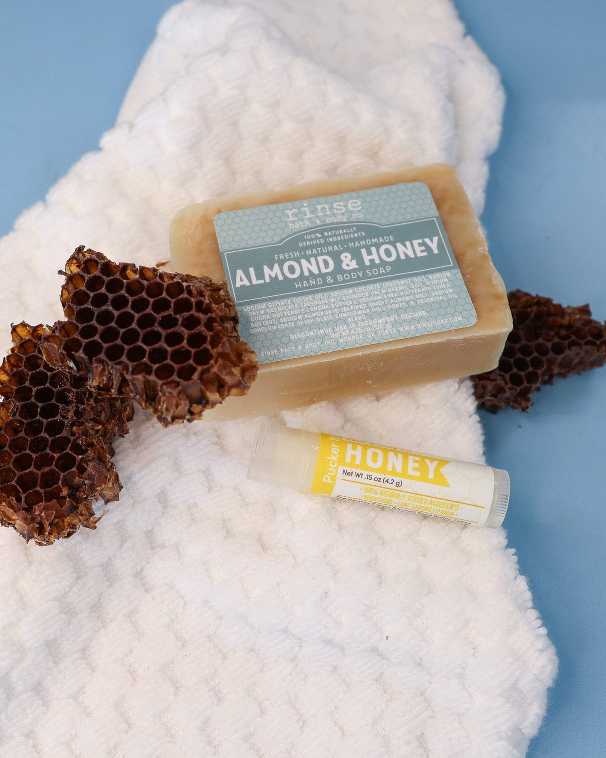 Almond & Honey bar and Honey Pucker Stick resting on a waffle towel with honeycomb — spa-calm blue surface in soft light