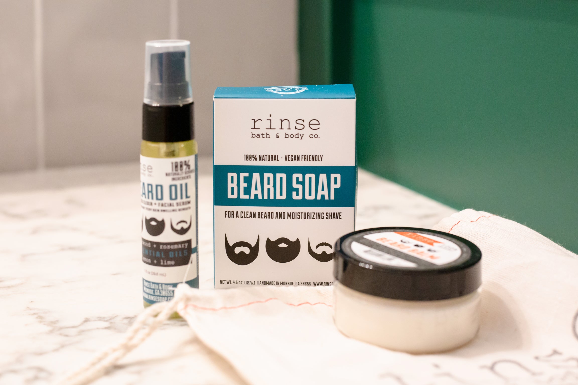 Rinse beard oil and beard soap styled on a marble tray against a green backdrop
