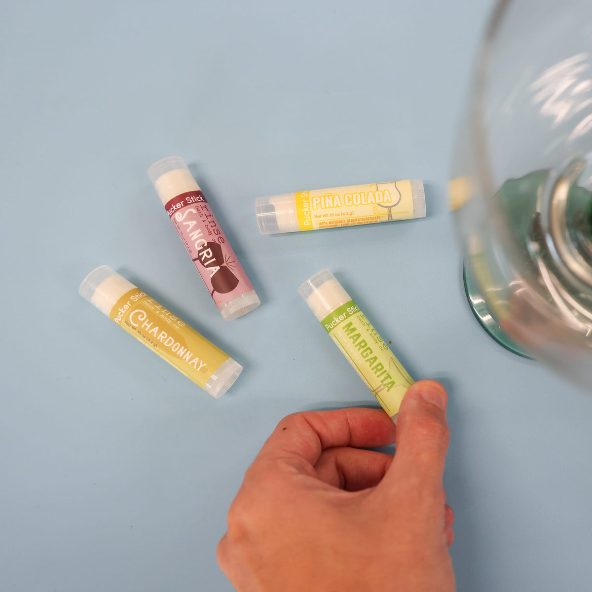 Hand picking Margarita Pucker Stick from Beverage Box set on light blue — Sangria Piña Colada Chardonnay nearby