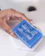 Orange-nailed fingers touching Blue Citrus soap on hexagonal marble — bright white vanity light