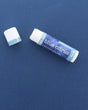 A Blue Citrus Skin Stick lying on a deep blue surface with its cap off, the twist-up solid lotion showing at the top — travel-friendly solid lotion in a pocket-sized tube. Rinse Bath & Body Co.
