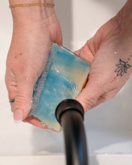 Hands lathering Blue Hawaiian soap under a black faucet — creamy white suds on blue marble bar