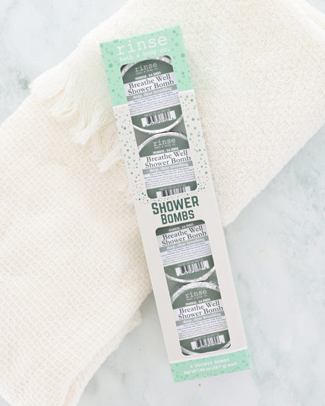 Breathe Well Shower Bomb 4-pack rests on a plush white towel, four (4) foil-wrapped shower bombs showing through the window, blended with peppermint, eucalyptus, thyme, sage and camphor.
