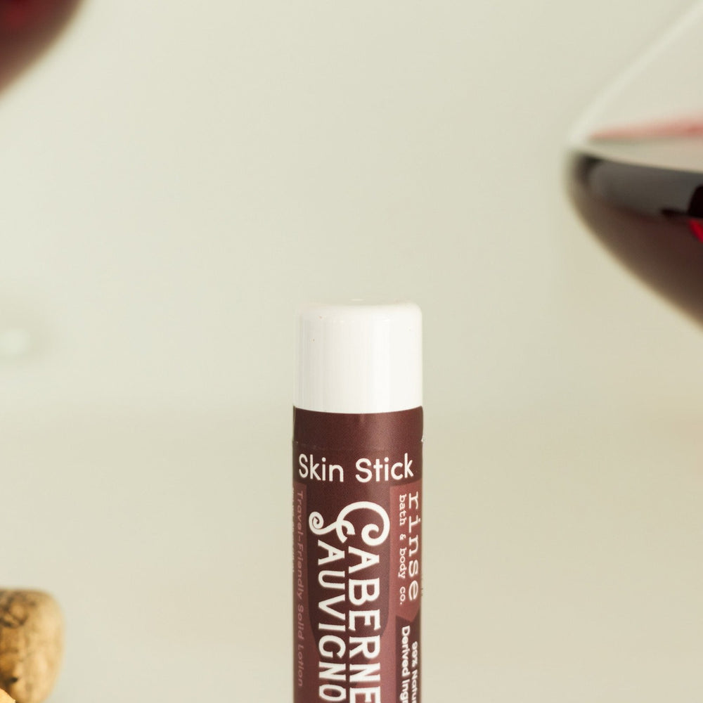 Cabernet Skin Stick standing beside cork, corkscrew, and cheese crumbs — wine-night solid lotion
