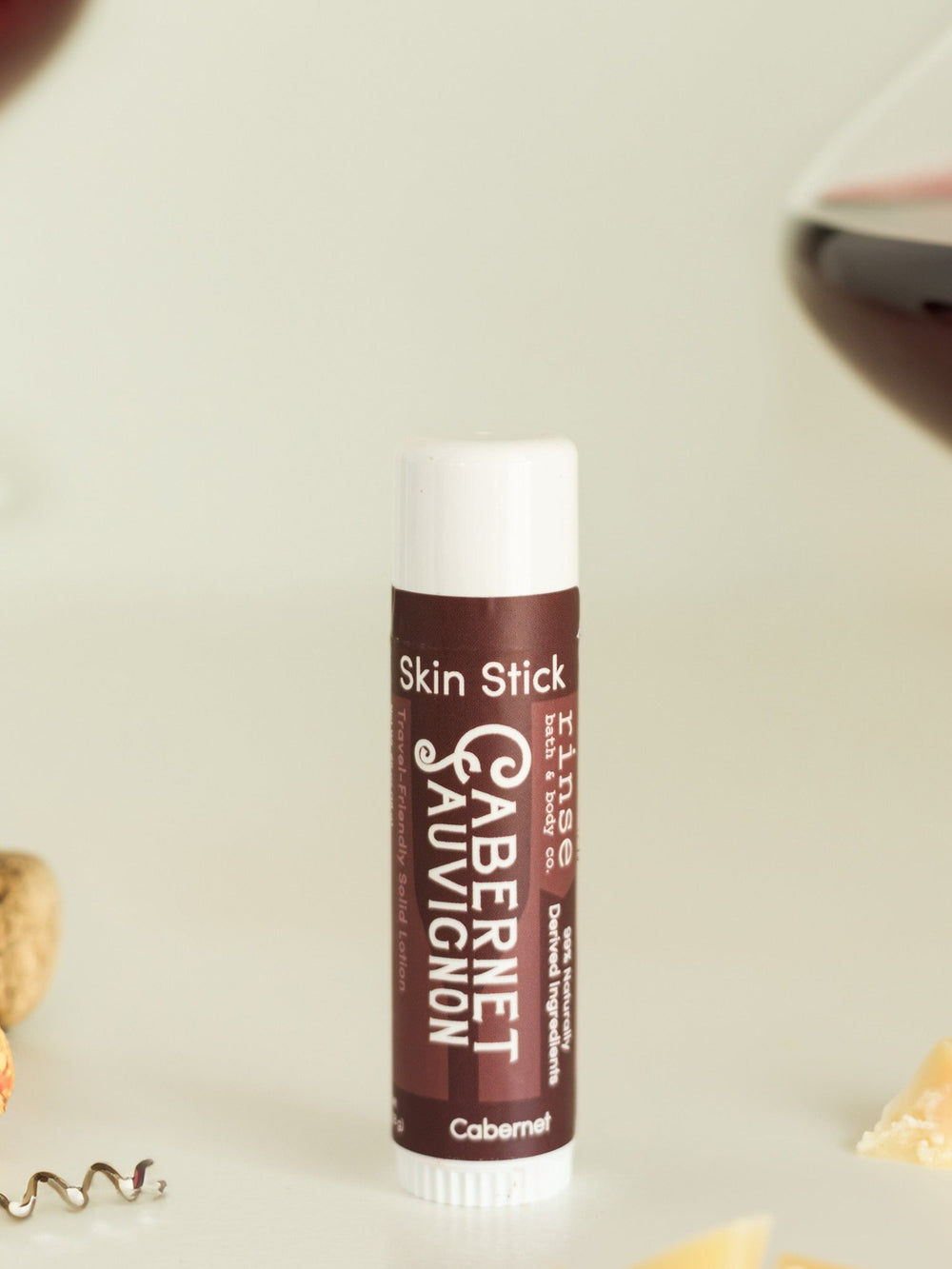 Cabernet Skin Stick standing beside cork, corkscrew, and cheese crumbs — wine-night solid lotion