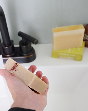 Hand rinsing Chardonnay bar soap under a matte black faucet — cream wine soap with botanical flecks in everyday shower cleanse