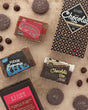 Chocolate soap gift set flat-laid with Chocolate Bar, Fudge Brownie, and Raspberry Drizzle beside diamond box and salted cookies