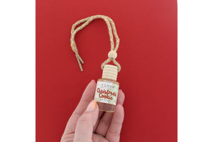 Hand holding Christmas Cookie car diffuser on saturated red — wood cap and jute cord in festive light