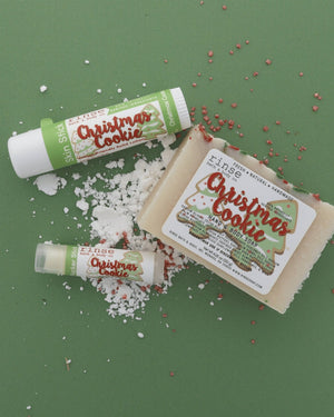 The Christmas Cookie gift set on sage paper scattered with snow and red-and-white sprinkles — bar soap, solid lotion skin stick and lip balm. Rinse Bath & Body Co.