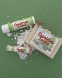 The Christmas Cookie gift set on sage paper scattered with snow and red-and-white sprinkles — bar soap, solid lotion skin stick and lip balm. Rinse Bath & Body Co.