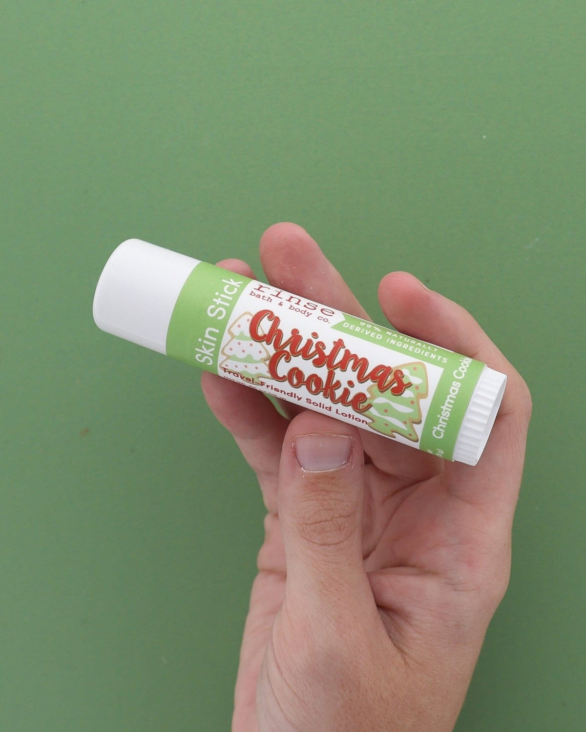 Hand holding Christmas Cookie Skin Stick on green — new cookie-label solid lotion gliding for dry winter hands