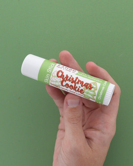 Hand holding Christmas Cookie Skin Stick on green — new cookie-label solid lotion gliding for dry winter hands