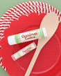 Christmas Cookie Skin Stick and Christmas Cookie Pucker Stick on a red scalloped plate with a wooden spoon