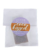 Coco Kissed soap slice in translucent glassine — orange-purple circle sticker on clean bright white