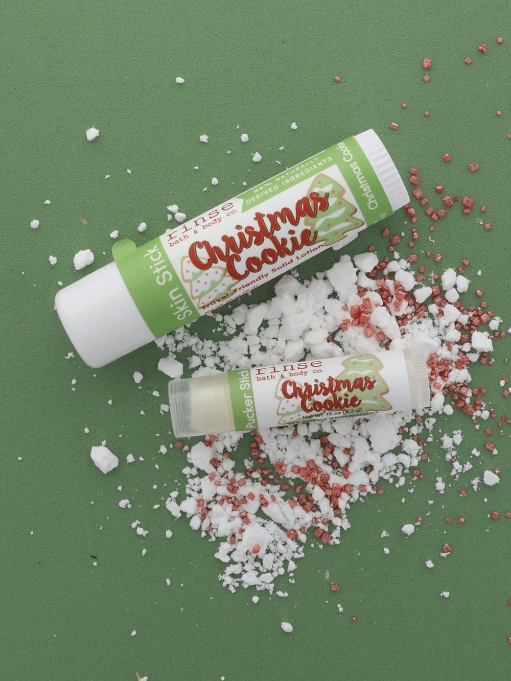 Christmas Cookie Skin Stick and Pucker Stick lifestyle on forest green — sugar crystals and bakery sprinkles