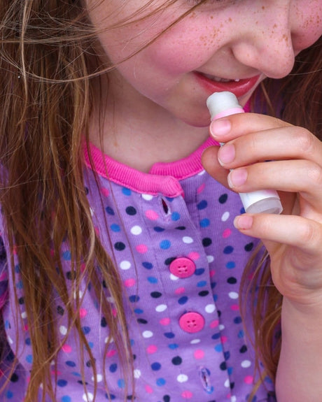 Smiling freckled girl applying Cotton Candy Pucker Stick — purple polka-dot shirt in soft natural light