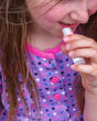 Smiling freckled girl applying Cotton Candy Pucker Stick — purple polka-dot shirt in soft natural light