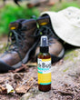 DeBug spray standing beside worn hiking boots and a canvas sun hat on a forest trail