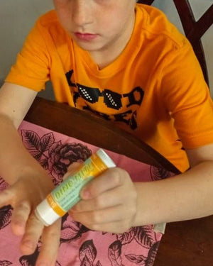 Boy in orange tee rubbing Dino-Mite Skin Stick onto his palm — soft solid lotion in daily use
