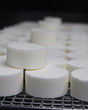Rows of freshly pressed white shower steamer pucks curing on a wire drying rack in the Monroe workshop — small-batch, pressed and cured by hand. Rinse Bath & Body Co.