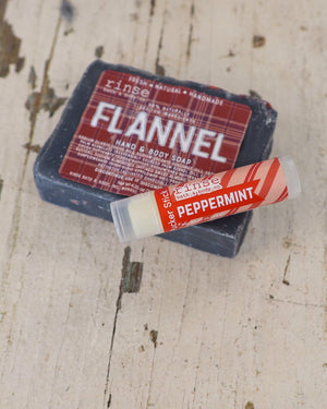 Dark Flannel soap with Peppermint Pucker Stick across its corner — weathered whitewashed wood in rustic light