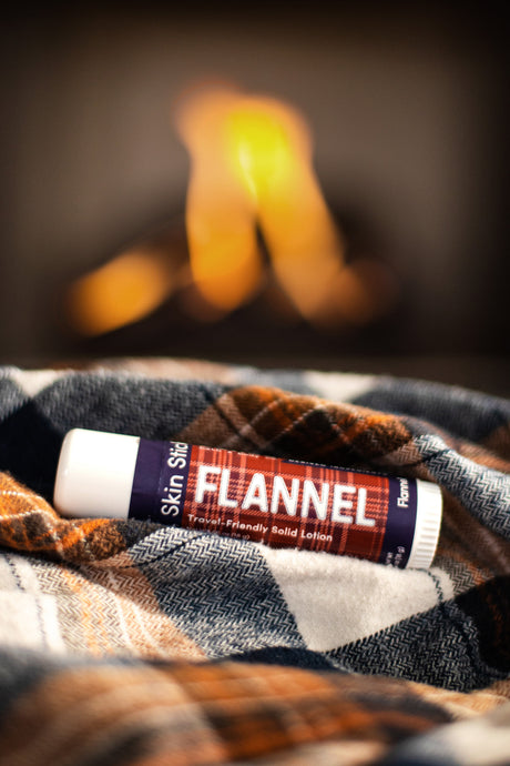 Flannel solid lotion stick resting on a plaid wool blanket in front of a lit fire — the cozy men's gift for cold hands and colder mornings. Rinse Bath & Body Co.