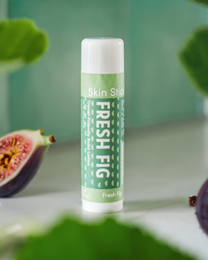 Fresh Fig Skin Stick standing beside a sliced pink fig on marble — travel-friendly solid lotion