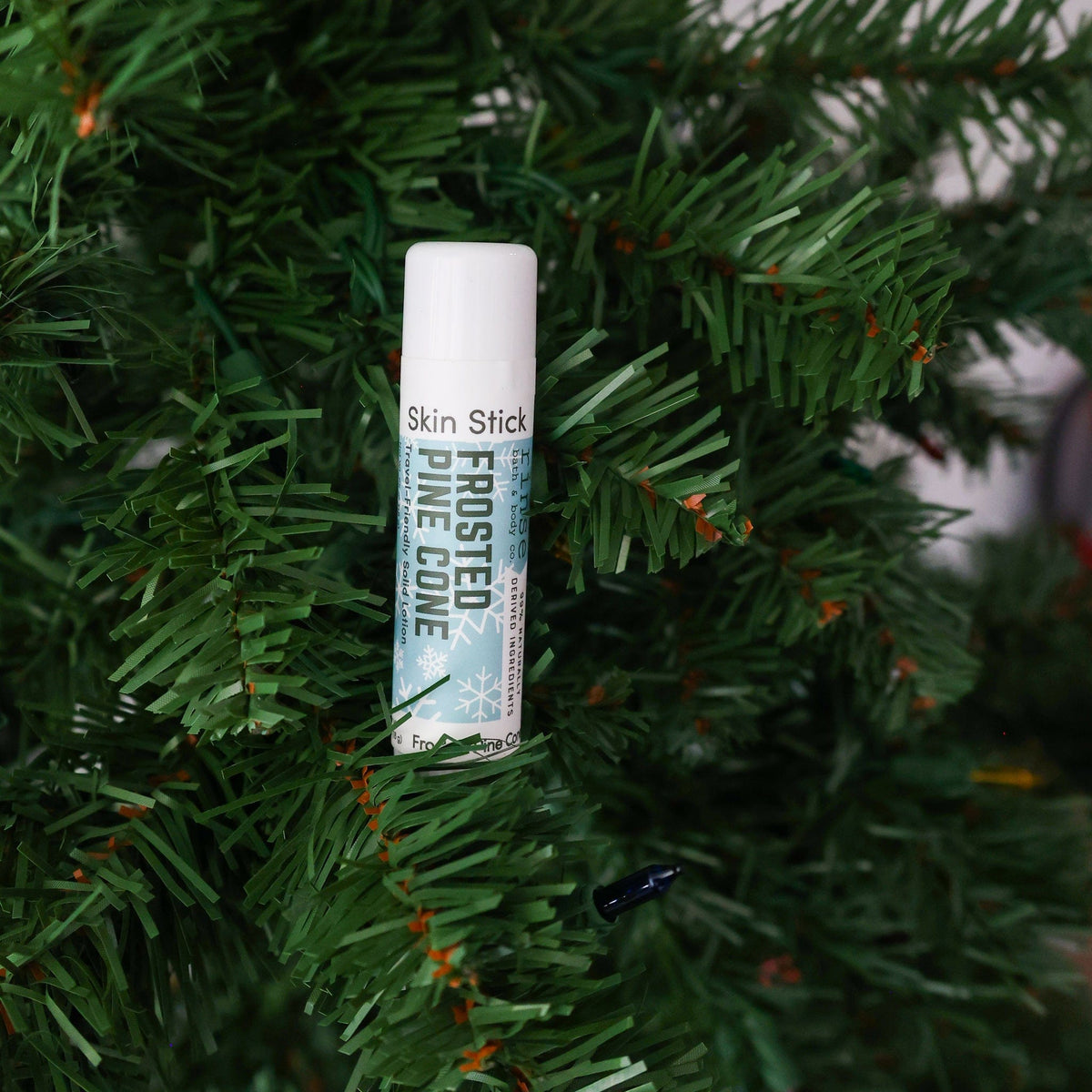 Frosted Pine Cone Skin Stick tucked among thick evergreen needles — deep green pine in outdoor light