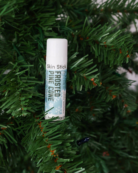 Frosted Pine Cone Skin Stick tucked among thick evergreen needles — solid lotion lifestyle in outdoor pine light