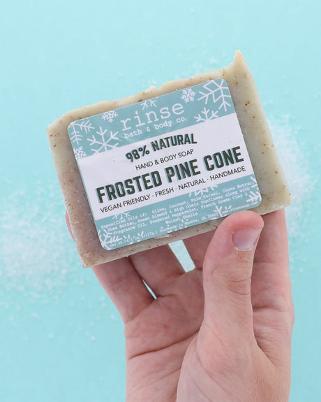 Hand holding Frosted Pine Cone soap over icy blue with crystal grains — frosty bar in use in cool studio light