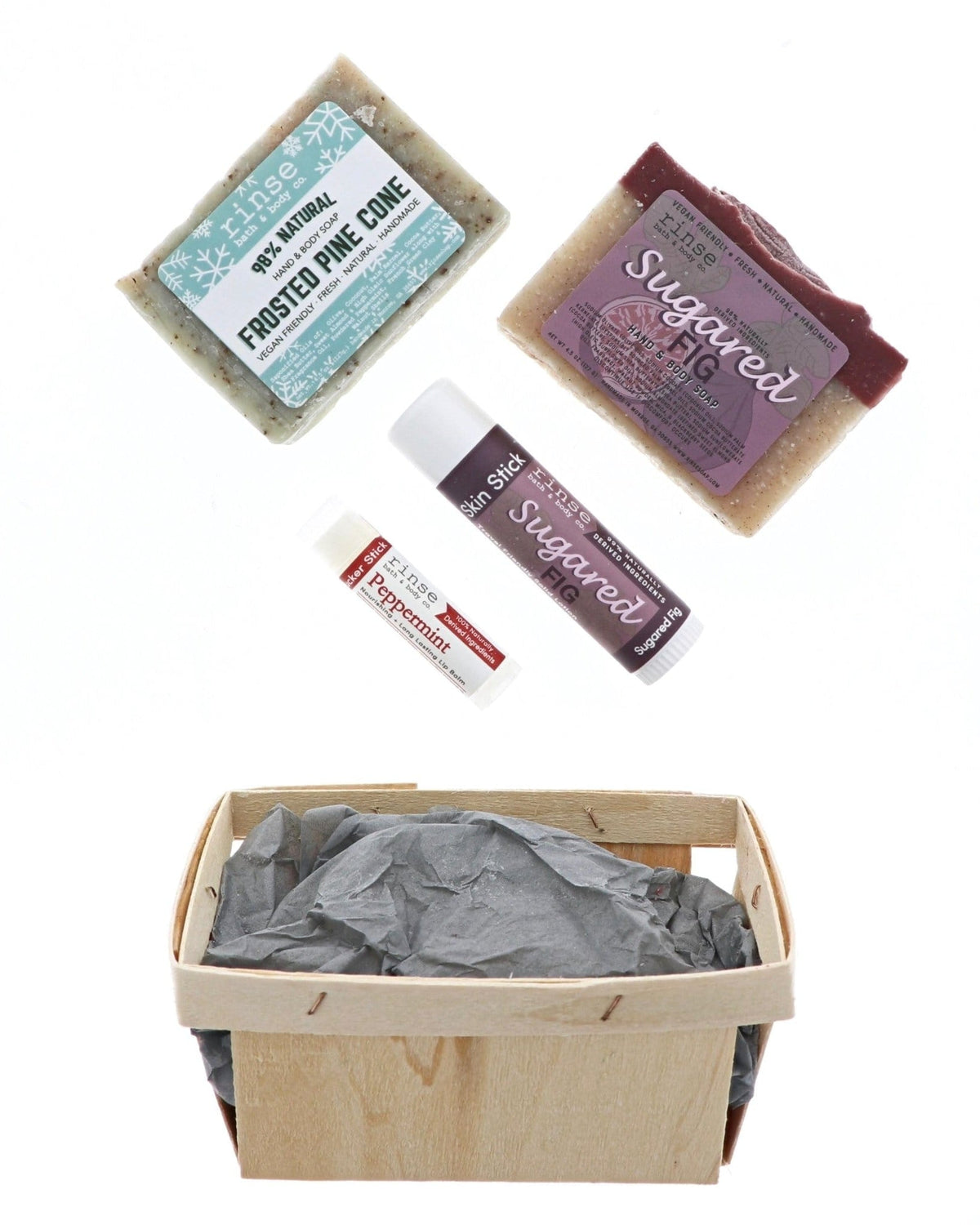 Holiday soaps Skin Stick and Peppermint balm floating above tissue-lined berry till — festive white studio space
