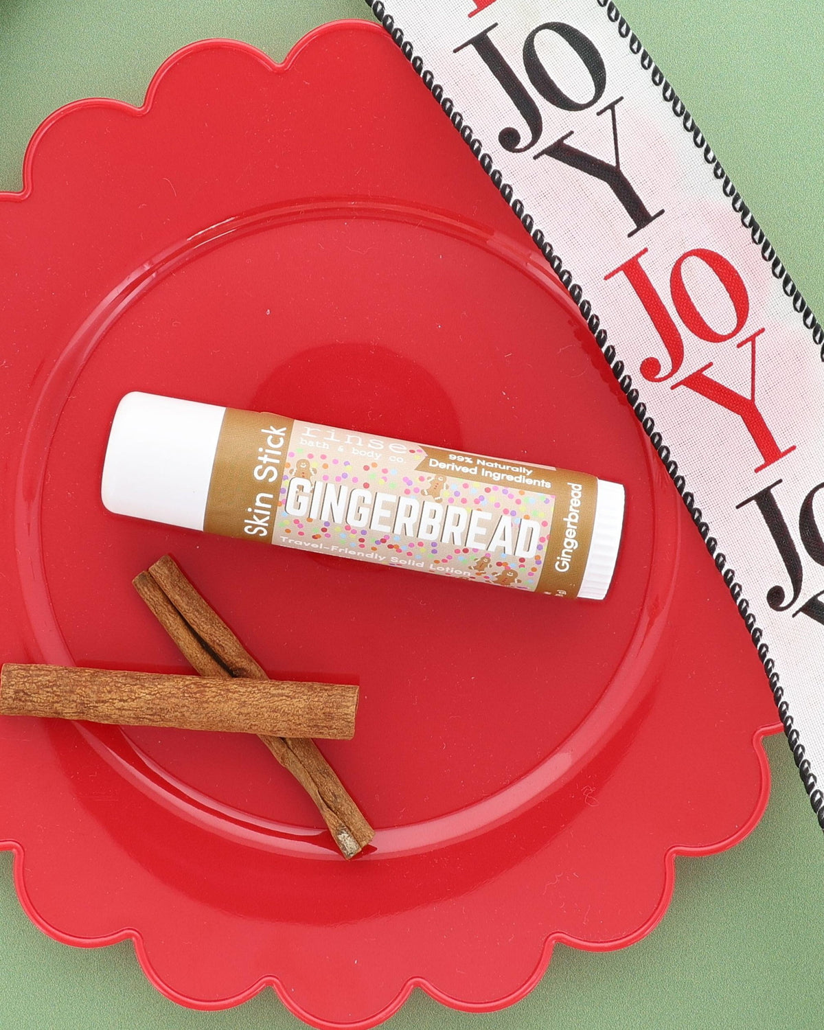 Gingerbread Skin Stick on a red scalloped plate with cinnamon sticks and a JOY ribbon on sage green