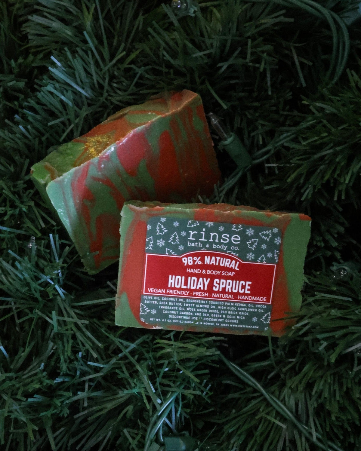 Holiday Spruce bar soap nestled in dense evergreen needles — red-green marble woodsy holiday soap