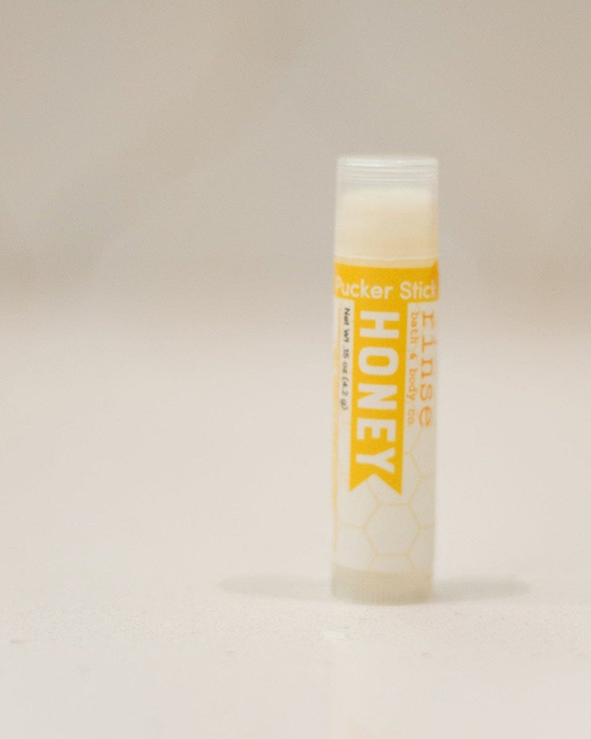 Honey Pucker Stick with its golden label, cap off — a twist-up balm that goes in a pocket and stays there. Rinse Bath & Body Co.