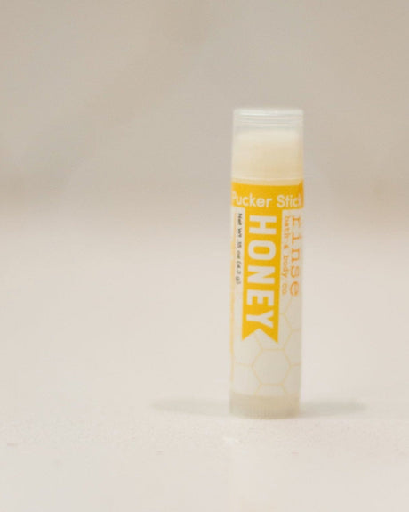 Honey Pucker Stick with its golden label, cap off — a twist-up balm that goes in a pocket and stays there. Rinse Bath & Body Co.