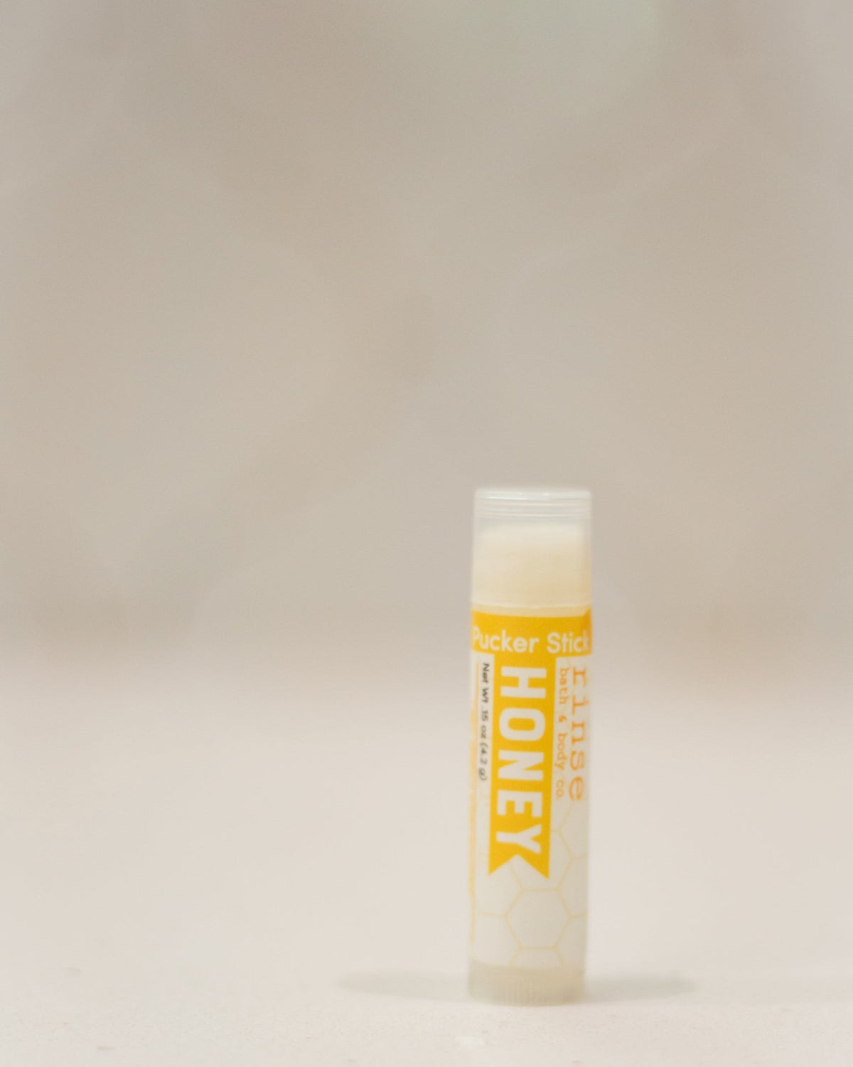 Honey Pucker Stick standing upright — yellow honeycomb label and clear cap on cream background