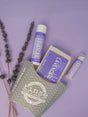 The Lavender gift set on lavender paper with dried lavender sprigs — bar soap, solid lotion skin stick and lip balm beside the grey chevron carton. Rinse Bath & Body Co.