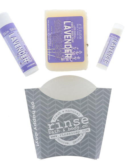 The Lavender set laid out flat — bar soap, Lavender solid lotion skin stick and Lavender lip balm above the grey chevron carton. Rinse Bath & Body Co.