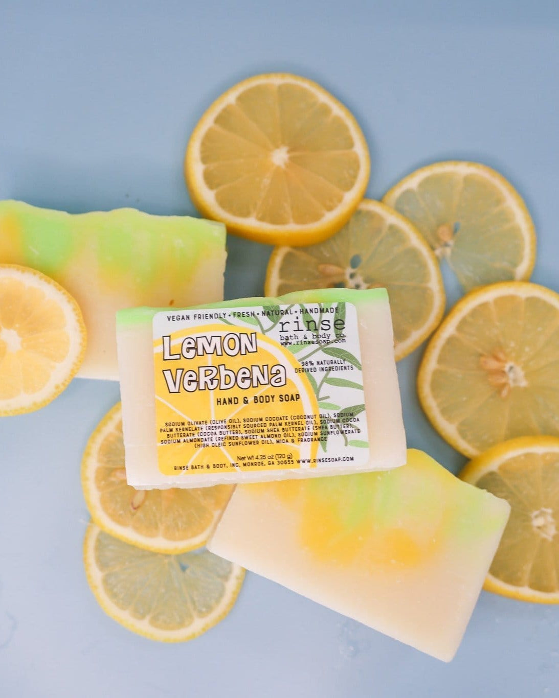 Lemon Verbena soap among fresh lemon slices — lime-yellow swirls on cool pastel blue flat-lay