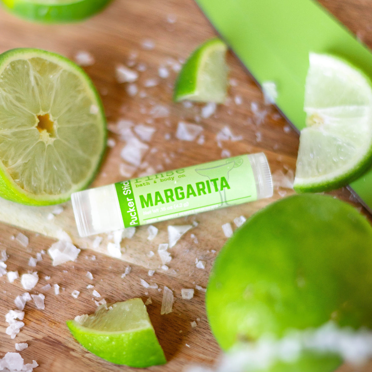 Margarita Pucker Stick lying on wood among lime wedges and coarse sea salt — zesty citrus props and warm cutting-board grain
