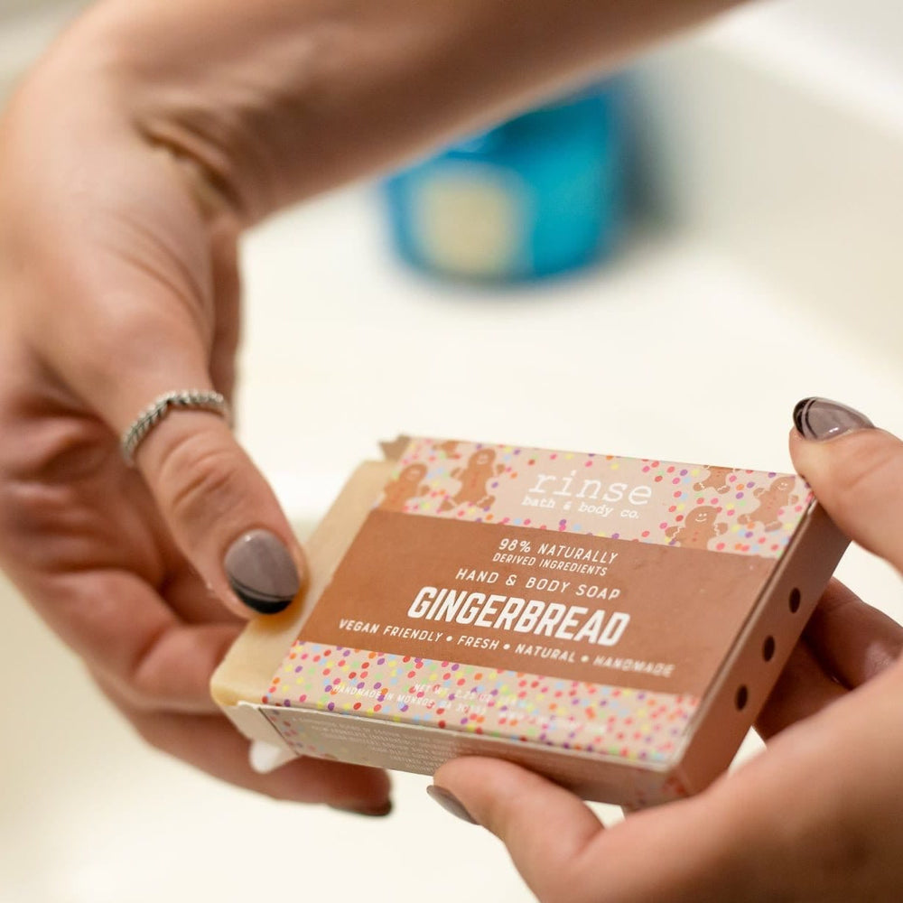 Hands sliding Gingerbread soap from its brown sleeve over a white sink — gold faucet soft in bathroom light